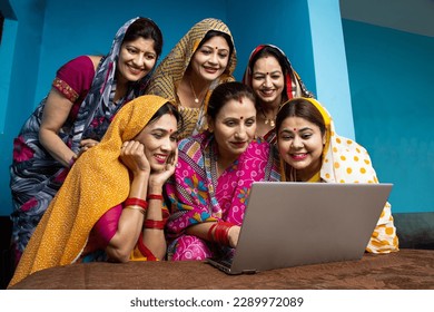 Group of young traditional indian women wearing sari learn to use laptop or computer. Technology in rural household. Concept of education and women empowerment.