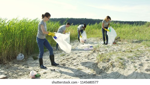 Group of young volunteers helping to keep nature clean and picking up the garbage from a sandy shore. - Powered by Shutterstock