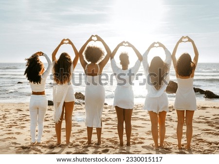 Group of young woman enjoying the sunset at the sea, doing hearth symbol with hands, standing in line, back view. Women celebrate hen party on coastline