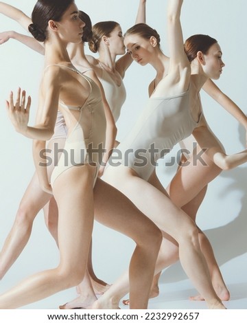 Group of young women, ballerinas dancing, performing isolated over grey studio background. Tender movements. Concept of art, beauty, aspiration, creativity, classic dance style, elegance
