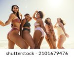 Group of young women dancing together in bikinis. Happy young women smiling cheerfully while dancing in swimwear. Carefree female friends having fun and enjoying their summer vacation at the beach.
