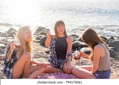 Group Of Young Women Friend Drinking Together A Fruit Juice On A Rock Beach In Tenerife. Relationship For A Team To Ejoy The Vacation And Happiness.