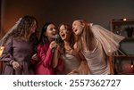 Group of young women friends and bride celebrating bachelorette party at home, bride and bridesmaids having fun, singing song in karaoke microphone.