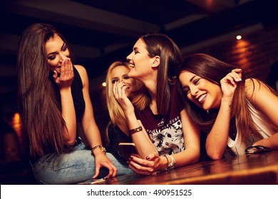 group of young women friends having fun looking at something funny on their smart phone and laughing - Powered by Shutterstock