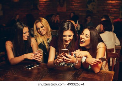group of young women friends having fun looking at something funny on their smart phone and laughing