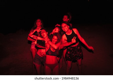 Group Of Young Women Having Fun At A Lakeside Party At Night With A Red Light