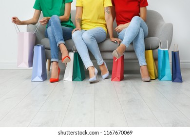 Group of young women with shopping bags sitting on sofa near light wall