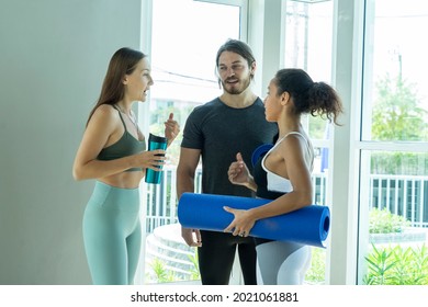 Group Of Young Women In Sportswear Holding A Thirst-quenching Water Bottle, A Male Trainer Talking To A Latin American Woman With A Yoga Mat Discussing Exercises At The Gym. 