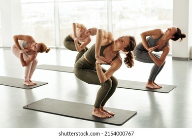 Group Of Young Women Standing On Yoga Mats And Doing Revolved Chair Pose At Class