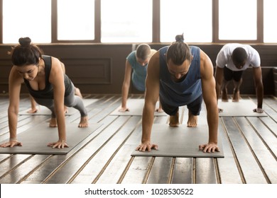 Group of young yogi people practicing yoga lesson standing in Plank pose, doing Push ups or press ups exercise, working out, indoor full length, studio floor - Powered by Shutterstock