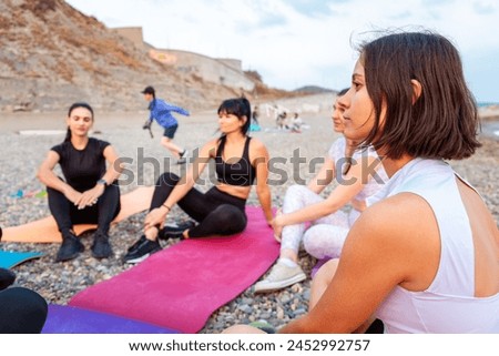 Group of young-adult multi-racial women are sitting on sports mats on wild beach and talking to each other. Concept of female circle of communication and outdoor yoga class.