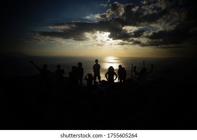 A groupie silhouette at the top of a mountain with the view of the ocean during sunset and dusk