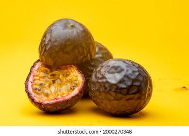 Grouping of Maracuja or Brazilian tropical passion fruit studio still life against a yellow background with one cut open showing the inside pulp flesh