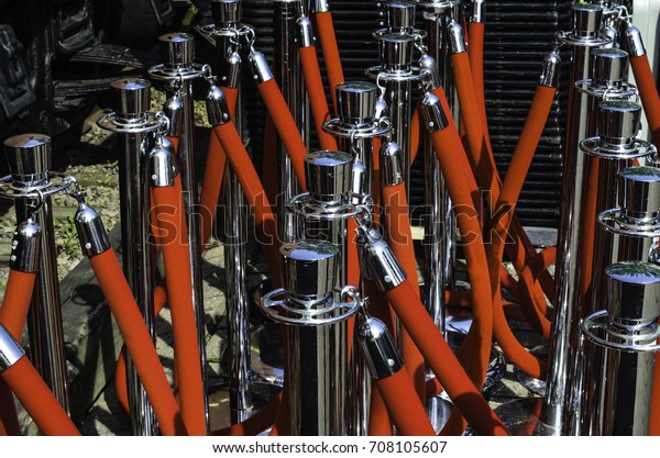 Grouping of rows of red velvet ropes\
and silver stanchions in the sunlight, waiting to be\
setup.