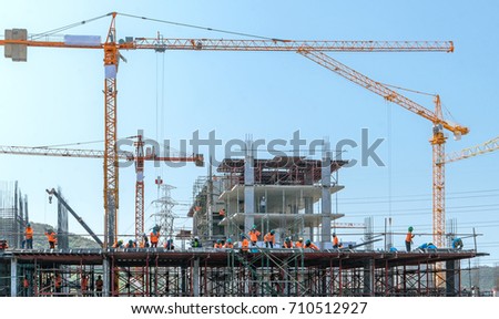 the grouping of workers  are working on construction site,labourers wearing safety helmet,construction crews on site,tower cranes