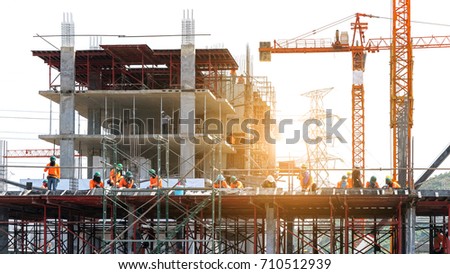 the grouping of workers  are working on construction site,labourers wearing safety helmet,construction crews on site with sunrise/sunset time,tower cranes