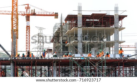 the grouping of workers  are working on construction site,labourers wearing safety helmet,construction crews on site with sunrise/sunset time,tower cranes