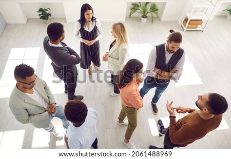 Groups of multi ethnic people standing in office and talking. Diverse men and women communicating during casual corporate meeting, psychological training or after business event. High angle shot