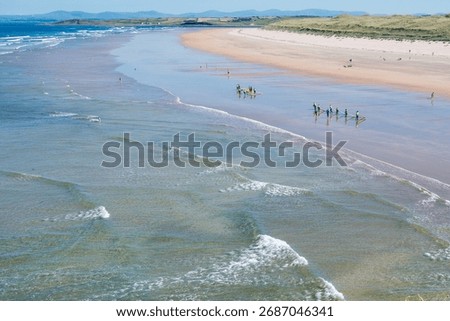 Groups of surfers navigate shallow waters at Finner Strand in Donegal, Ireland, enjoying sunny skies and a peaceful atmosphere while preparing for their surfing adventures.