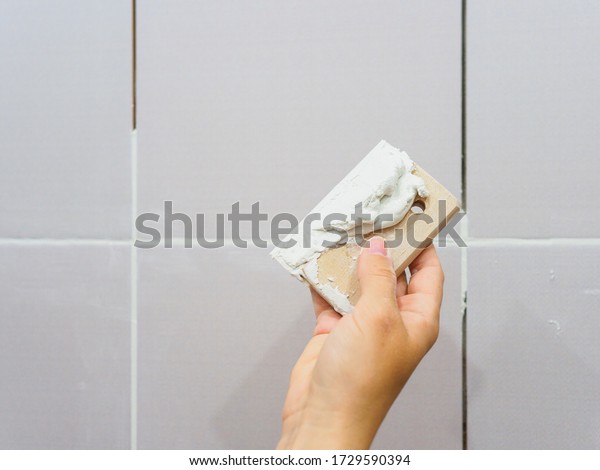 Grouting between tiles in the bathroom. Female\
hand holds a spatula.\
Repairs.
