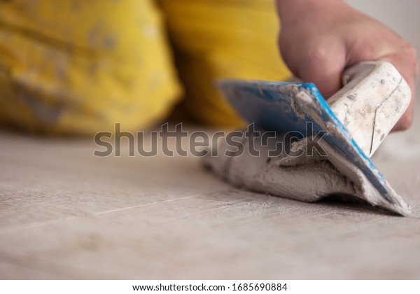 Grouting ceramic tiles. Tilers filling the\
space between ceramic wood effect tiles using a rubber trowel on\
the floor in new modern\
apartment