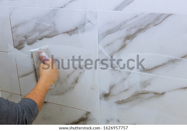 Grouting tiles male hand with the rubber applies\
grout on a seam between\
tiles