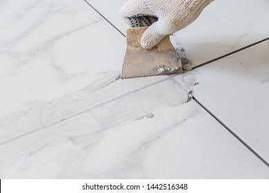 Grouting tiles seams with a rubber trowel. - Shutterstock ID 1442516348