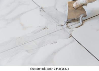 Grouting tiles seams with a rubber trowel. - Shutterstock ID 1442516375