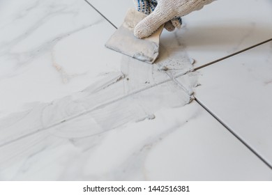Grouting tiles seams with a rubber trowel. - Shutterstock ID 1442516381