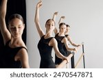 Growing skills before performance. Teen beautiful girls, ballet dancers standing at barre and practicing with concentration against grey studio background. Concept of ballet, art, dance studio, youth