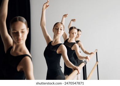 Growing skills before performance. Teen beautiful girls, ballet dancers standing at barre and practicing with concentration against grey studio background. Concept of ballet, art, dance studio, youth - Powered by Shutterstock