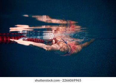 Growing speed and strength. Young woman, professional swimmer in goggles and cap training in swimming pool. Underwater view. Concept of sport, endurance, competition, energy, healthy lifestyle - Shutterstock ID 2266069965