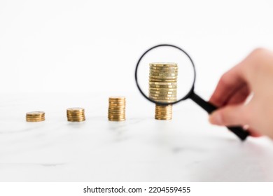 growing stacks of coins with magnifying glass analysing them, conceptual image about increasingly expensive prices or savings and compound interests - Shutterstock ID 2204559455