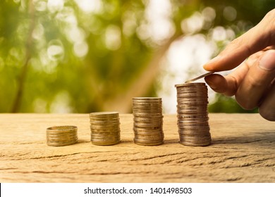 Growing time value of money, investment, wealth financial concept. Hand holding coin on rising stacked coins on wooden table. Long term sustainable fund, passive income for long term financial growth.