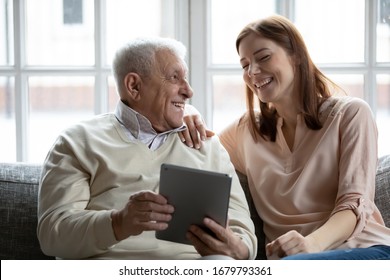 Grown up daughter her old father spend time resting on couch at home. Older man holding tablet device, with adult granddaughter using e-commerce website, do shopping in internet store together concept - Powered by Shutterstock