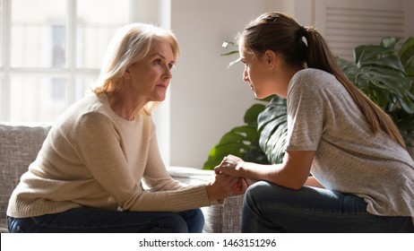 Grown up daughter holding hands of middle aged mother relatives female sitting look at each other having heart-to-heart talk, understanding support care and love of diverse generations women concept