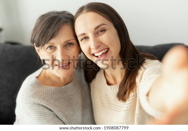 A grown daughter and a senior elderly\
mother takes a selfie, two smiling multigenerational women looks at\
the camera cheerfully, record\
themself