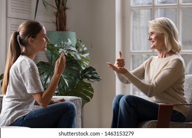 Grown up daughter talk with middle aged mother people using sign language, family sitting on armchair side view, teacher teach teenager deaf-mute girl to visual-manual gestures symbols concept image