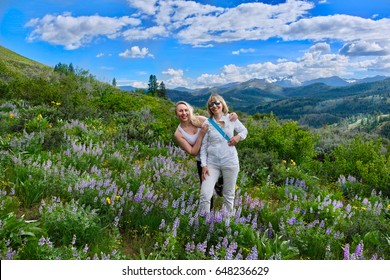 Grown Up Family Hiking In Meadows With Wildflowers. Young Daughter And Middle Age Mother Smiling In  Banff National Park. Canadian Rockies. Calgary. Alberta. Canada.