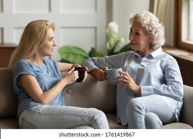 Grown up millennial daughter enjoy pleasant conversation with aged mother, different generations women having warm relations, spend time together drinking hot beverage in cozy home atmosphere concept