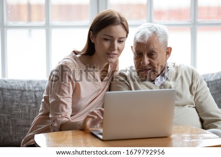 Grown-up daughter and old 80s father choose goods or services via internet or web surfing together at home. Younger generation caring about older relatives teaching using computer useful apps concept