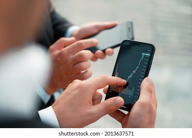 Growth charts on stock markets. Male brokers hold phones in their hands. Cryptocurrency trading on the stock exchange