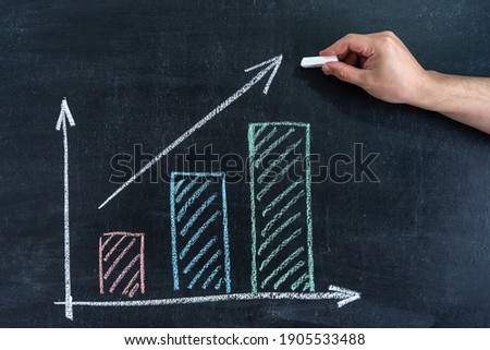 Growth graph on a chalk board. Man's hand with white chalk draws an upward arrow