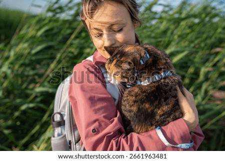 Grumpy curious cat frowns while inspecting grass nature from woman owner arms. Feline curious and cautious exploration, animal comfort zone dependence, reluctant adventurer feel discomfort and stress