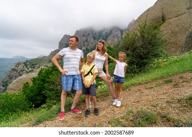 Grumpy Family With Kids In Green Meadow Looking At Valley. Concept Of Family Travel In Mountains. Father, Mother, Daughter And Son Have Fun In Nature