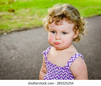 Grumpy hot ,sweaty little girl at the park on a hot day, dropping her bottom lip.