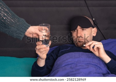 Grumpy Man in Bed with a Headache and Hangover Takes Water and Painkiller from His Wife