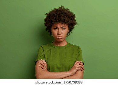 Grumpy offended millennial woman holds hands crossed on chest, frowns face, has quarrel with someone, angry expression, wears green t shirt, being mad at you, feels insulted, unwilling to talk - Shutterstock ID 1750738388