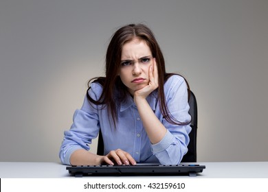 Grumpy Young Woman Using Computer Keyboard On Grey Office Desktop