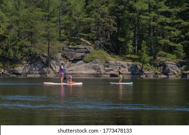 Grundy Provincial Ark, Ontario, Canada - Jul 4, 2020: Family In Life Vests Paddle Boarding On A Stand Up Board . Summer Activities And Water Sports. Space For Copy.